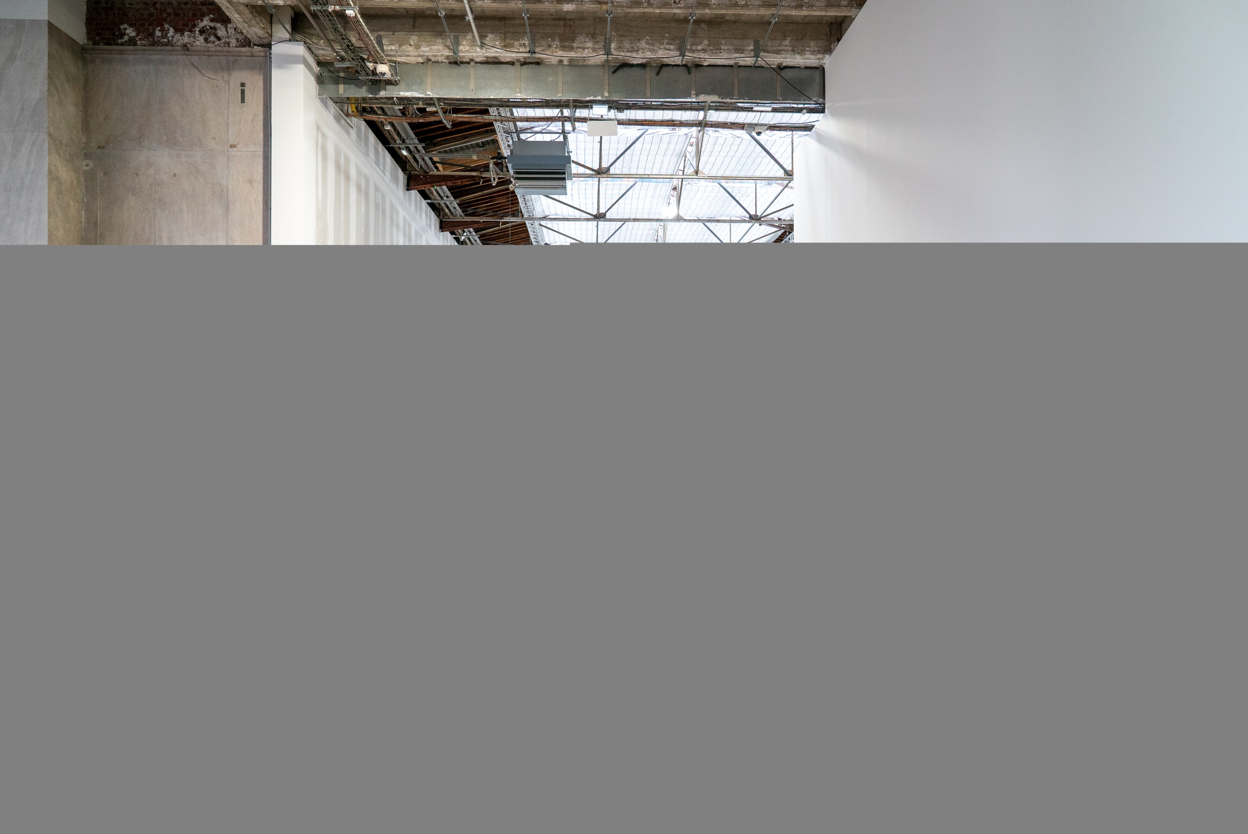 Dans l’un des espaces d’expositions du Palais de Tokyo, le démontage en cours, inaccessible au public, laisse apercevoir de grands panneaux de bois brut, d’autres recouverts de peinture noire. Sur le côté, des plateformes élévatrices et des chariots permettent de transporter outils et matériaux.