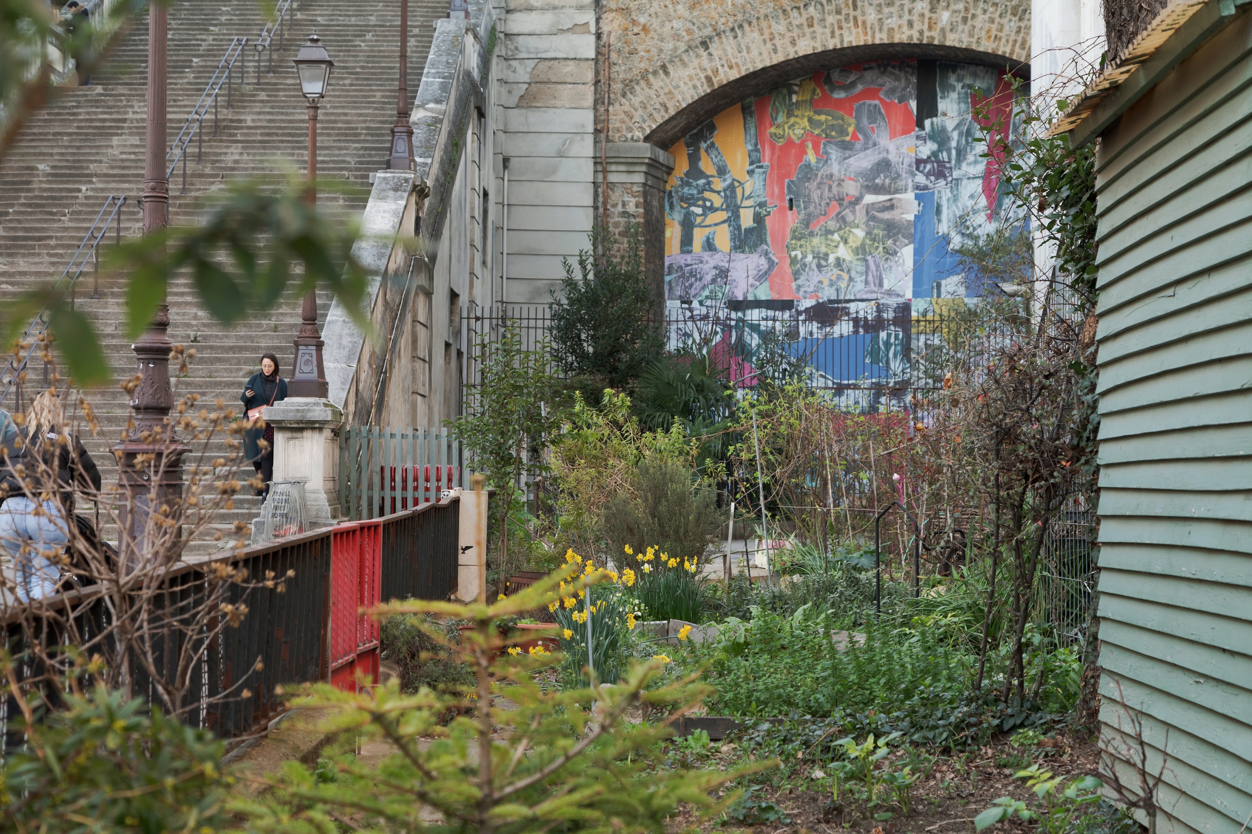 Les petites parcelles qui constituent le jardin aux habitants sont entourées de clôtures métalliques et sont parsemées de petites cabanes de jardin. Au fond de la rue, les escaliers remontent vers l’avenue, et une fresque géante aux couleurs vives marque l’entrée du jardin sauvage. 