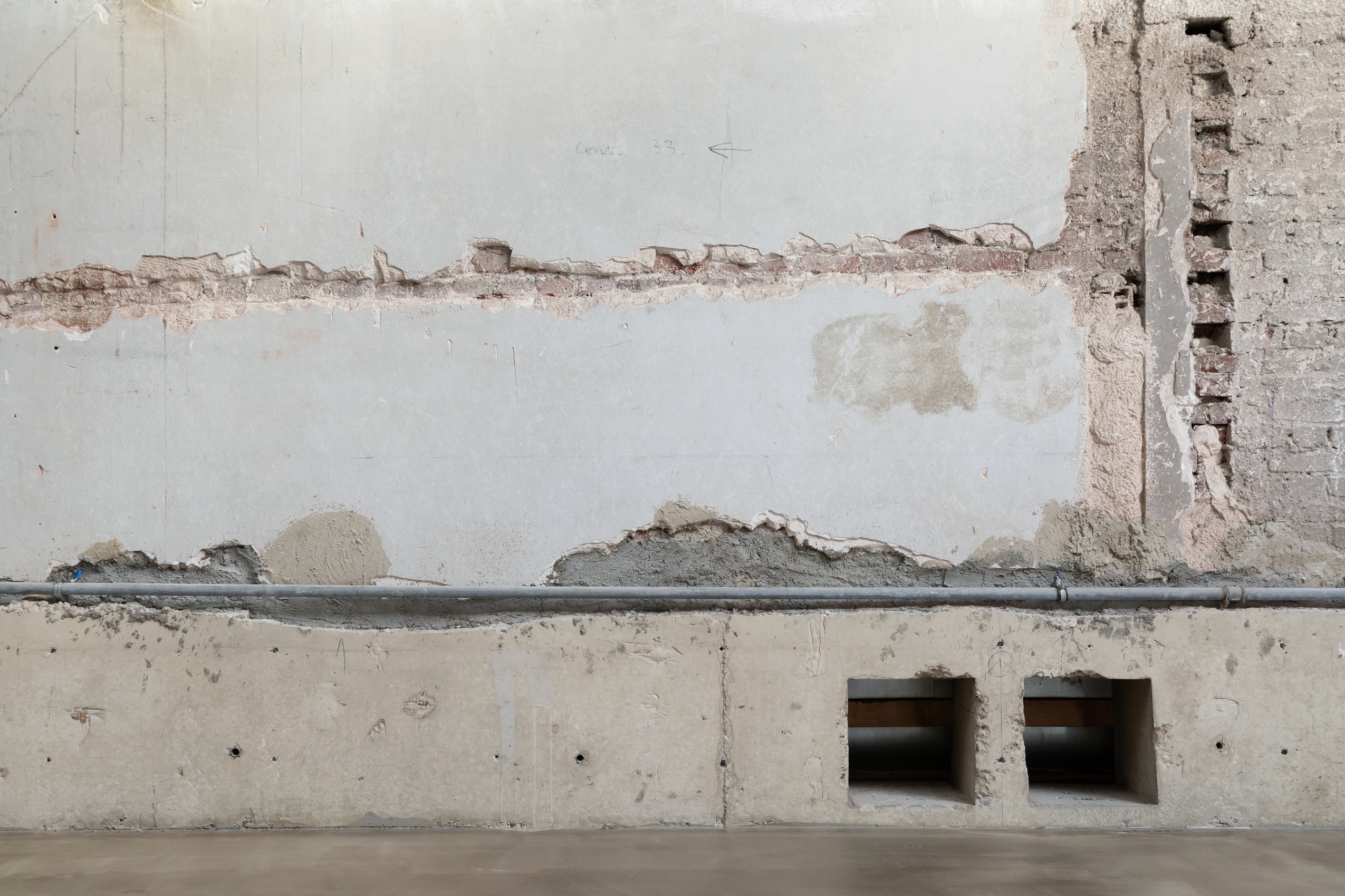 Les murs de la salle Toguna sont un patchwork de matériaux, entre briques, béton, enduits, peinture et infrastructures techniques comme des tuyaux et câbles.